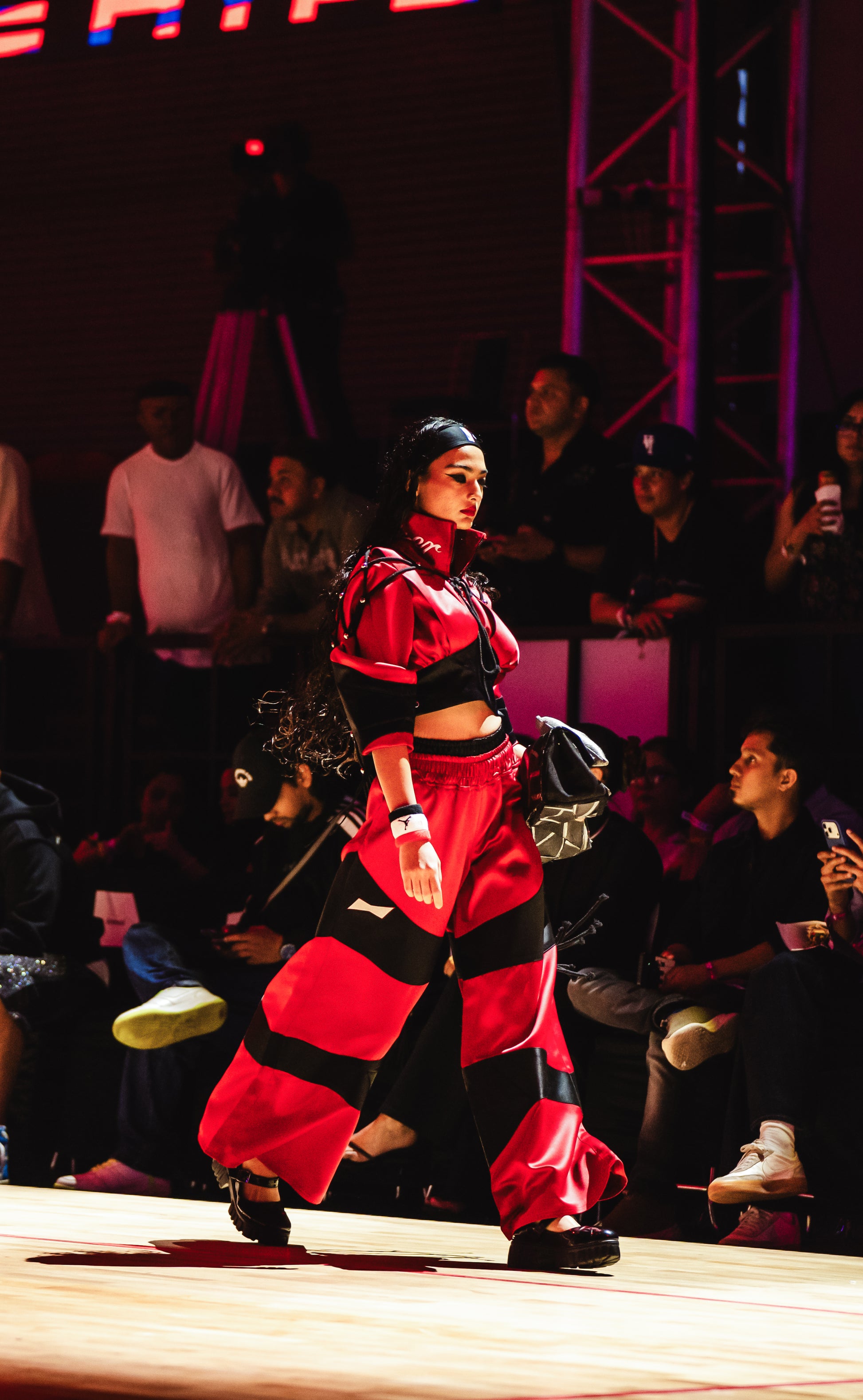 Model walking on a runway at a BUDXNBAHOUSE fashion show wearing Satine Red Black Sweatpants.